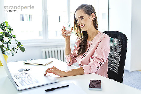 Lächelnde junge Frau arbeitet am Laptop im Home-Office