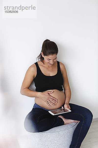 Junge schwangere Frau mit Ultraschallbild ihres ungeborenen Babys auf der Tablette