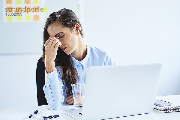 Junge Frau sitzt mit Kopfschmerzen im Büro