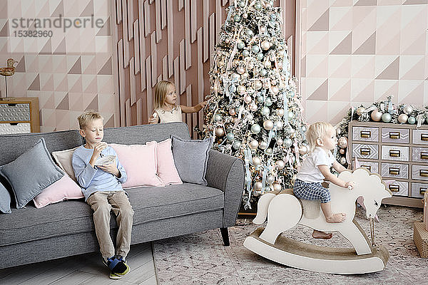 Drei Kinder  die zur Weihnachtszeit im Wohnzimmer spielen und Kekse essen