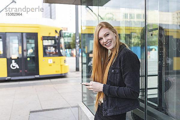 Porträt einer rothaarigen jungen Frau mit Smartphone in der Stadt  Berlin  Deutschland