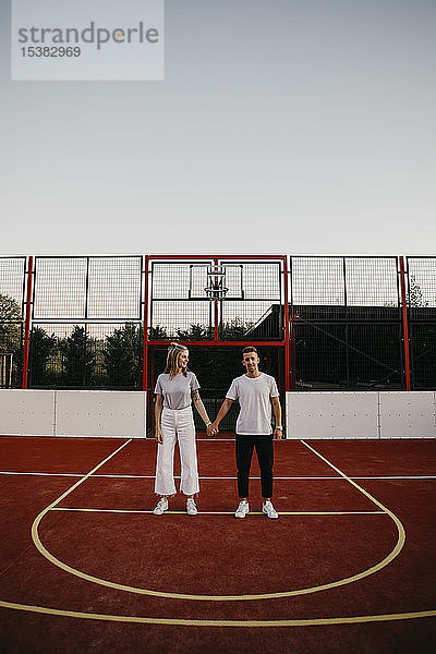 Junges Paar auf einem Basketballplatz  Händchen haltend