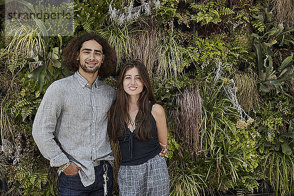 Porträt eines lächelnden jungen Paares vor einer Pflanzenwand