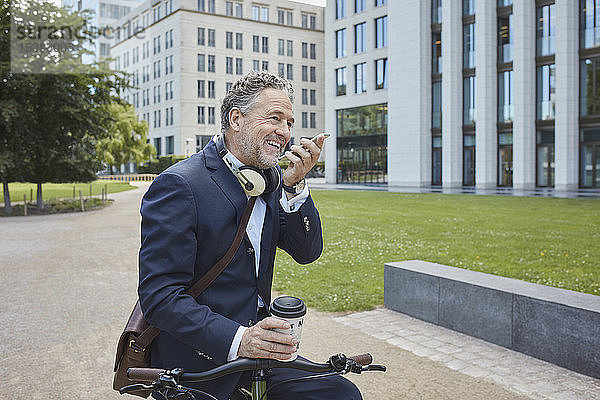 Älterer Geschäftsmann mit Fahrrad und Smartphone in der Stadt
