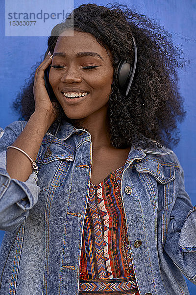 Porträt einer lächelnden jungen Frau  die mit Kopfhörern Musik hört