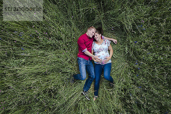 Schwangere Frau und Mann halten Babybauch  liegen auf der Wiese