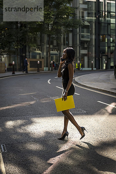 Geschäftsfrau überquert Straße und benutzt Smartphone in der Stadt