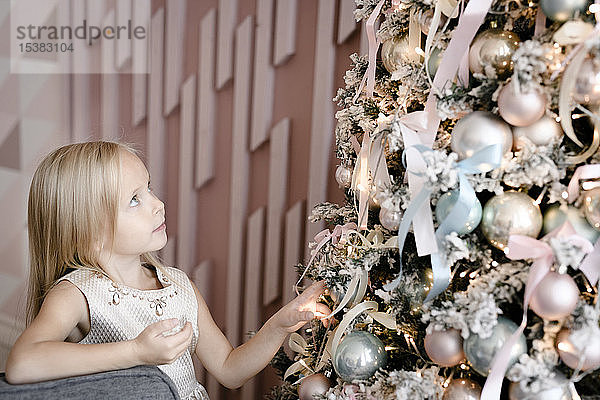 Blondes kleines Mädchen beobachtet Weihnachtsbaum
