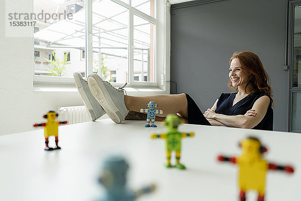 Porträt einer rothaarigen Frau in einem Loft mit Miniaturrobotern auf dem Schreibtisch