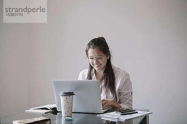 Lächelnde junge Frau  die am Tisch im Büro mit einem Laptop arbeitet