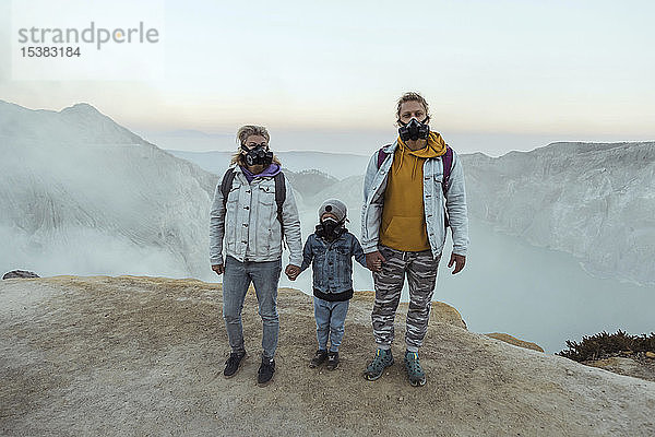 Familie mit Atemschutzmasken steht Hand in Hand am Rande des Vulkans Ijen  Java  Indonesien