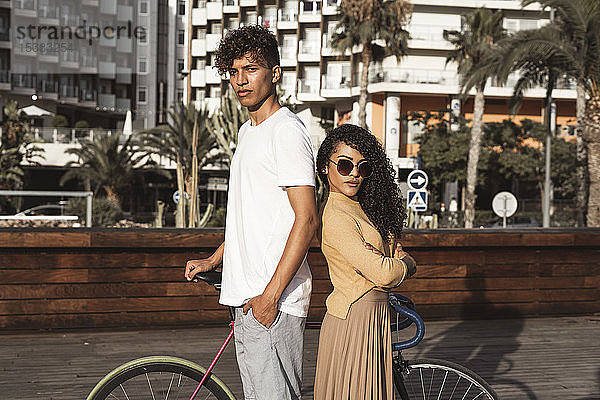 Cooles Paar mit Fahrrad in der Stadt  Rücken an Rücken stehend