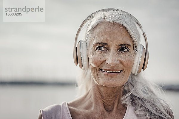 Ältere Frau beim Musikhören mit Kopfhörern am Meer  poartrait