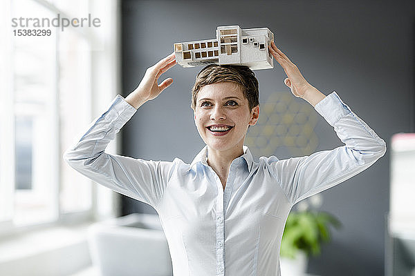 Glückliche Geschäftsfrau trägt Architekturmodell auf dem Kopf