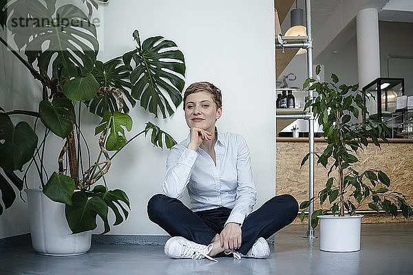 Porträt einer Geschäftsfrau  die auf dem Boden sitzend von Pflanzen umgeben ist