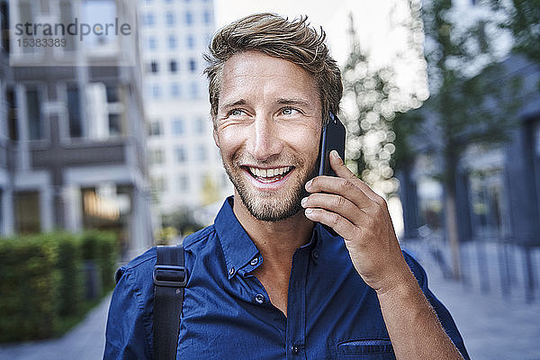 Porträt eines glücklichen jungen Geschäftsmannes am Telefon in der Stadt