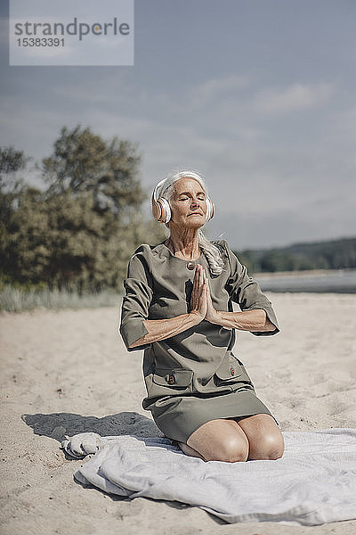 Ältere Frau meditiert mit Kopfhörern am Strand