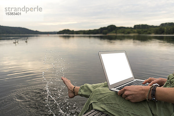 Junge Frau mit Laptop auf einem Steg an einem See