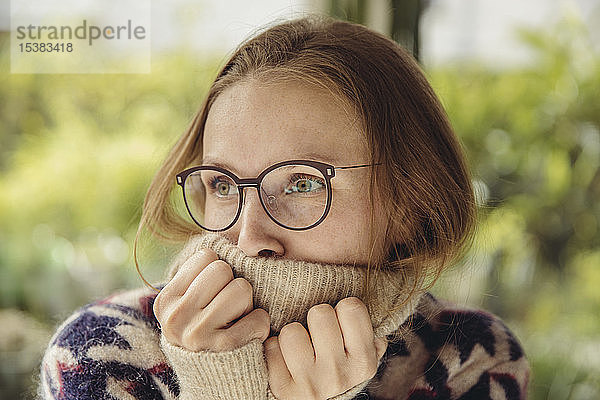 Junge Frau mit Brille  die einen flauschigen Pullover trägt und zur Seite schaut