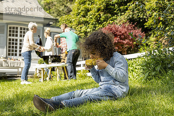 Junge isst einen Maiskolben auf einem Familiengrill im Garten