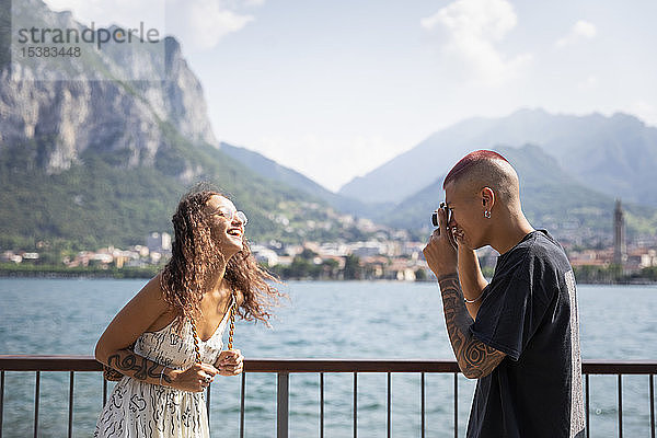 Junger Mann fotografiert seine Freundin vor dem Comer See  Lecco  Italien