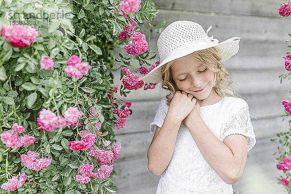 Bildnis eines lächelnden Mädchens mit geschlossenen Augen am Rosenbusch