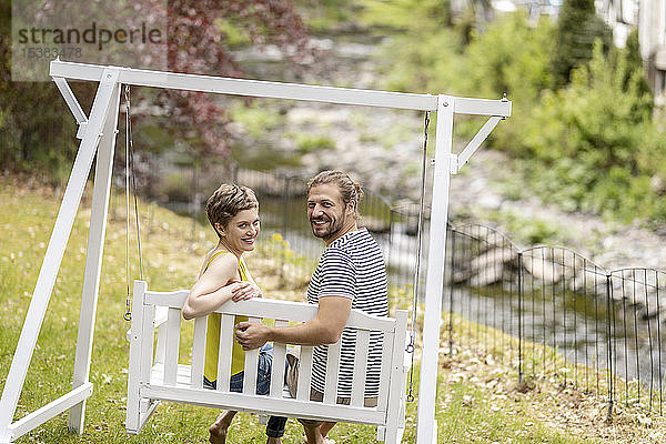 Porträt eines lächelnden Paares  das auf einer Baldachinschaukel im Garten sitzt