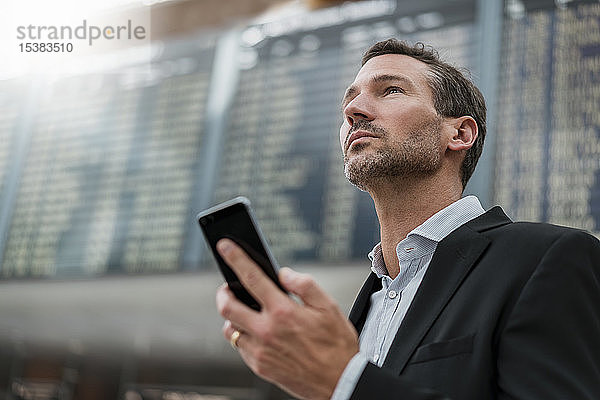 Porträt eines Geschäftsmannes mit Handy bei der Ankunft Abflugtafel am Flughafen