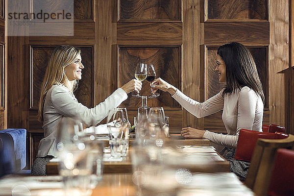 Zwei Geschäftsfrauen klirren in einem Restaurant an einem Weinglas