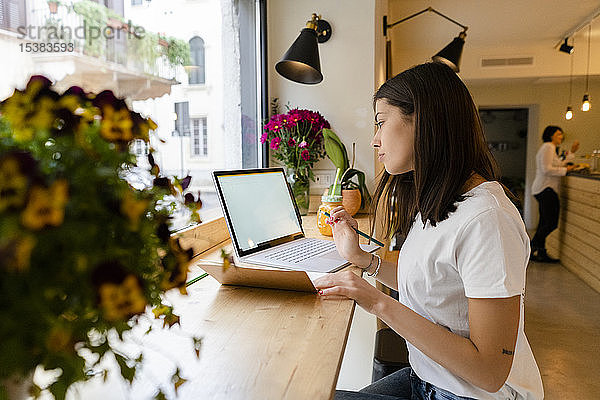 Junge Frau benutzt Laptop und macht Notizen in einem Cafe