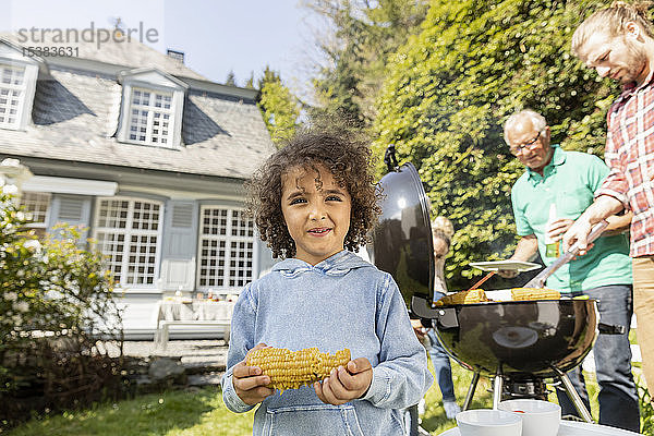 Porträt eines Jungen mit Maiskolben auf einem Familiengrill im Garten