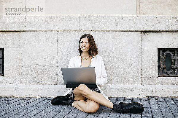Geschäftsfrau  die in der Stadt am Boden sitzt und einen Laptop benutzt