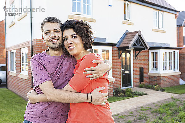 Porträt eines glücklichen Paares  das sich vor seinem neuen Zuhause umarmt