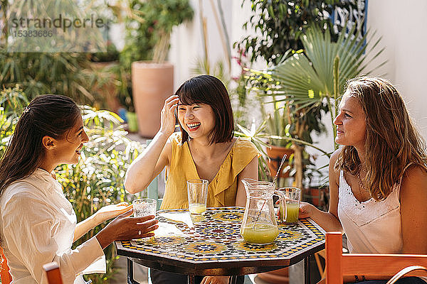 Drei glückliche Freundinnen treffen sich in einem Café und trinken Limonade