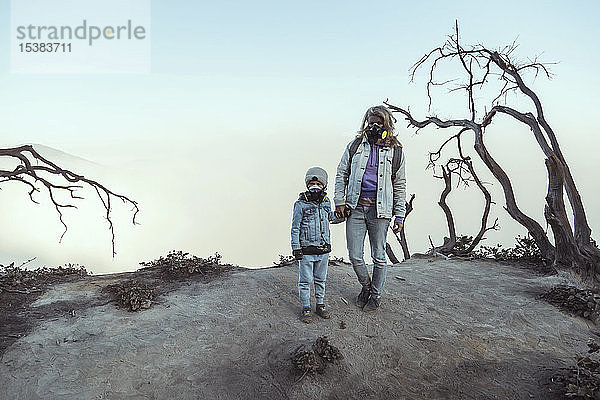 Mutter und Sohn mit Atemschutzmasken stehen Hand in Hand am Rande des Vulkans Ijen  Java  Indonesien