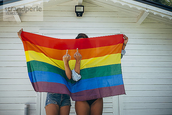 Zwei Frauen zeigen den Finger vor einer Regenbogenfahne