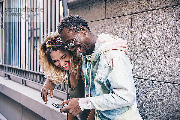 Lachendes Paar benutzt Mobiltelefon im Freien