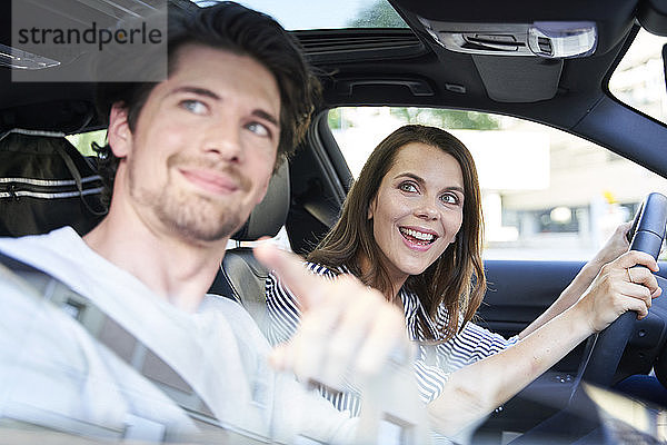 Glückliches Paar in einem Auto mit Frau am Steuer und Mann  der mit dem Finger zeigt