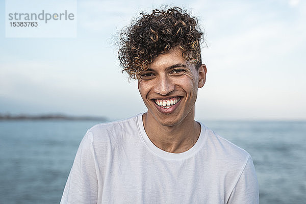 Porträt eines lachenden jungen Mannes mit lockigem Haar am Meer