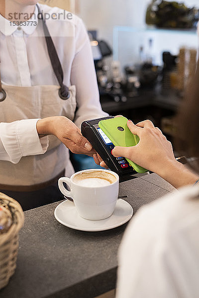 Nahaufnahme eines bargeldlos mit Smartphone zahlenden Kunden in einem Cafe