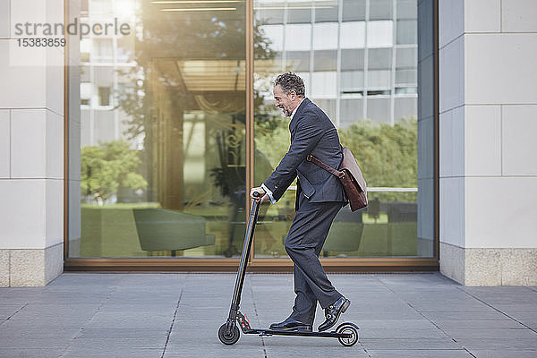 Geschäftsmann auf E-Scooter fährt an Bürogebäude in der Stadt vorbei