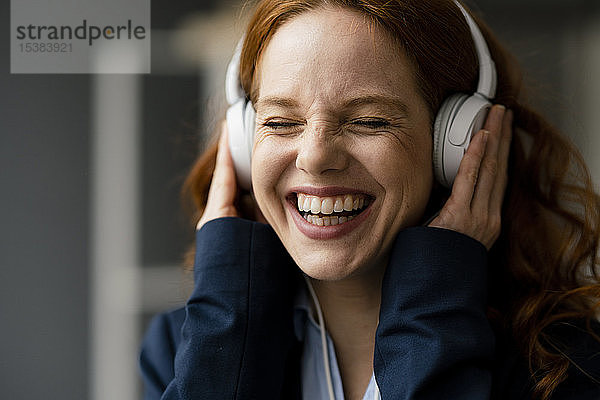 Porträt einer lachenden rothaarigen Geschäftsfrau  die mit weißen Kopfhörern Musik hört