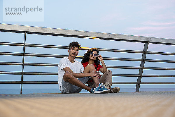 Junges Paar auf der Brücke am Meer sitzend