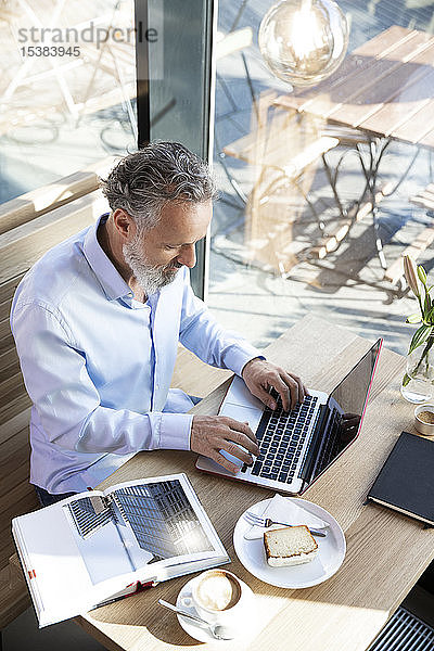 Reifer Mann mit Laptop in einem Café mit Buch auf dem Tisch