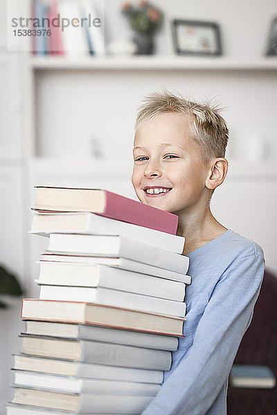 Porträt eines lächelnden blonden Jungen  der einen Stapel Bücher trägt