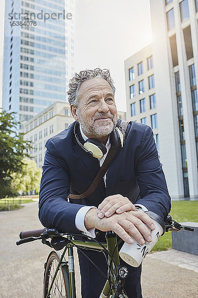 Reifer Geschäftsmann mit Fahrrad und Kaffee zum Mitnehmen in der Stadt