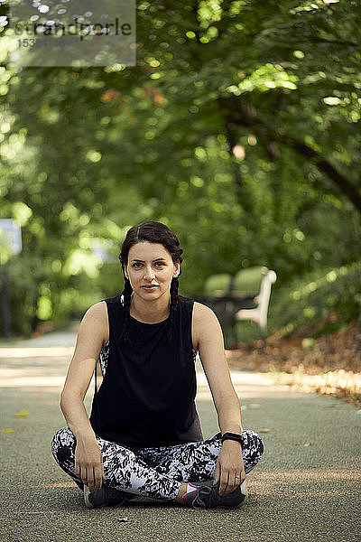 Porträt einer sportlichen jungen Frau am Waldweg sitzend