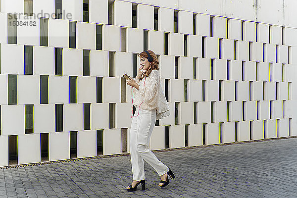 Geschäftsfrau geht auf die Straße und hört mit Kopfhörern Musik von ihrem Smartphone