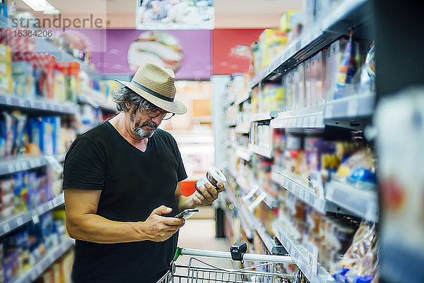 Älterer Mann kauft mit seinem Smartphone in einem Supermarkt ein
