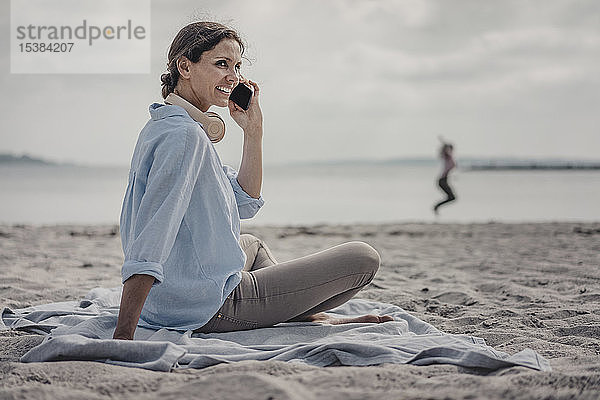 Frau sitzt am Strand und telefoniert